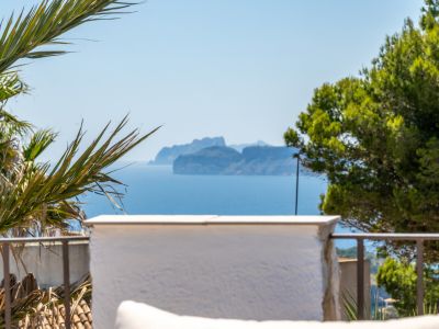 Vue panoramique sur la mer avec une île montagneuse lointaine, encadrée par une végétation méditerranéenne et une balustrade de terrasse.