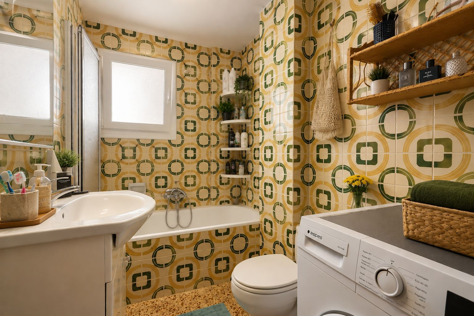 La salle de bain complète arbore un carrelage distinctif à motifs géométriques jaunes et verts, un lavabo avec meuble, une baignoire avec pare-douche et une machine à laver intégrée, éclairée par une fenêtre dépolie.