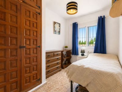 Chambre confortable avec armoire encastrée en bois à panneaux décoratifs et ferrures noires. Fenêtre avec rideaux bleus et vue sur la verdure, apportant lumière naturelle.