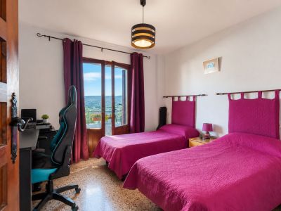 Chambre lumineuse avec deux lits simples, têtes de lit fuchsia et accès direct à un balcon avec vue sur la montagne. Comprend un coin bureau et un sol en terrazzo.