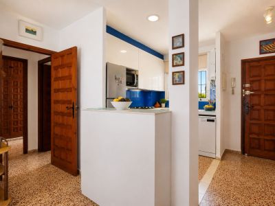Le hall d'entrée présente un carrelage à motifs distinctifs et des portes en bois classiques. Une cuisine moderne avec crédence bleue et meubles blancs est visible, séparée par un comptoir fonctionnel.