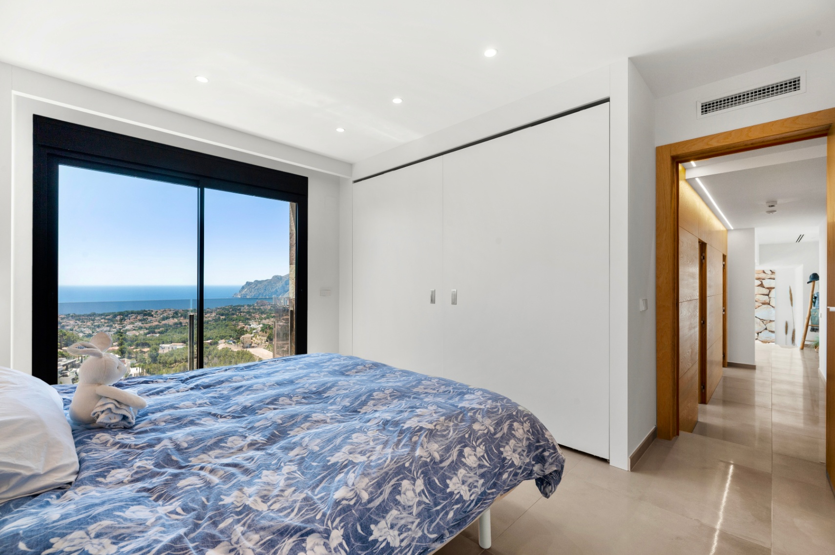 Chambre avec portes coulissantes vitrées pleine hauteur, offrant des vues panoramiques sur la mer et la ville. Intègre des armoires blanches encastrées et un sol carrelé clair. Chambre avec portes coulissantes vitrées pleine hauteur, offrant des vues panoramiques sur la mer et la ville. Intègre des armoires blanches encastrées et un sol carrelé clair.