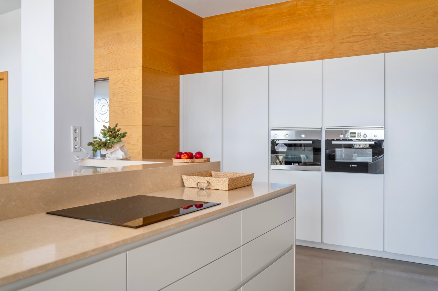 Cuisine moderne avec plan de travail couleur sable et plaque à induction intégrée. Deux fours Bosch encastrés et un mur décoratif en bois clair. Cuisine moderne avec plan de travail couleur sable et plaque à induction intégrée. Deux fours Bosch encastrés et un mur décoratif en bois clair.
