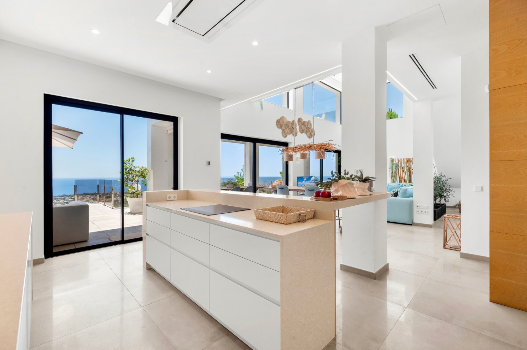 Cuisine ouverte moderne avec îlot central en comptoir beige et plaque à induction intégrée. De larges baies vitrées coulissantes offrent une vue directe sur la mer Méditerranée, éclairant l'espace contemporain. Cuisine ouverte moderne avec îlot central en comptoir beige et plaque à induction intégrée. De larges baies vitrées coulissantes offrent une vue directe sur la mer Méditerranée, éclairant l'espace contemporain.