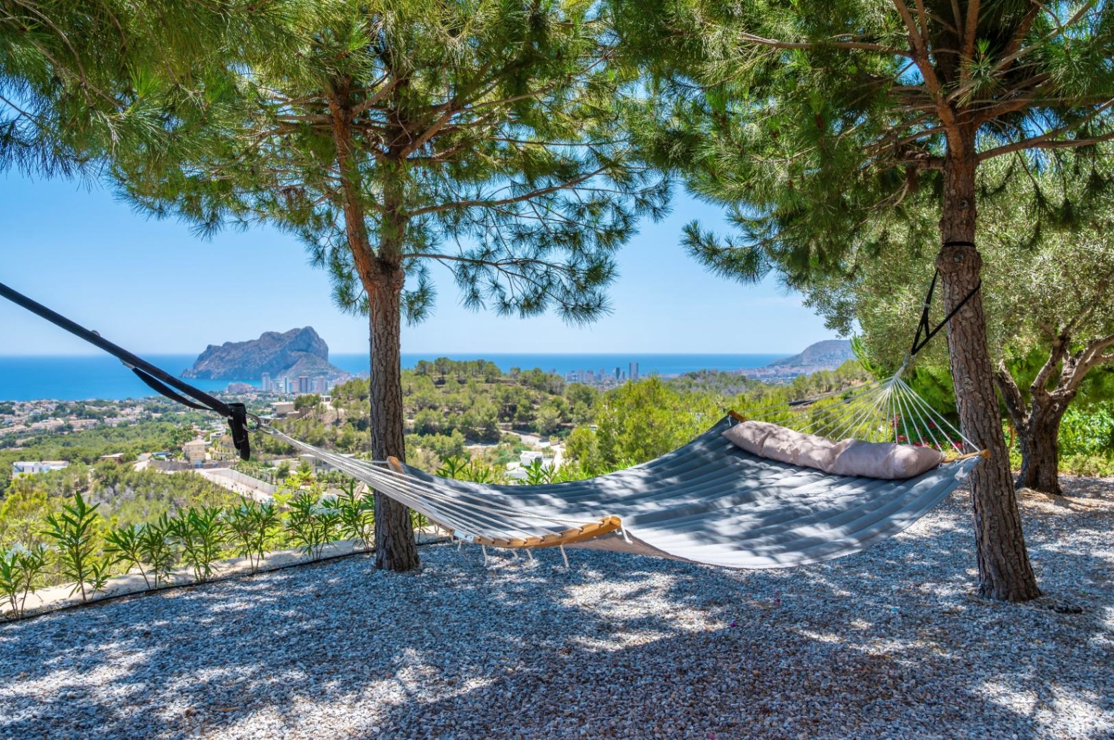 Hamac rembourré installé sous les pins, offrant un espace de détente avec des vues panoramiques sur la mer Méditerranée et le majestueux Peñon de Ifach. Sol en gravier. Hamac rembourré installé sous les pins, offrant un espace de détente avec des vues panoramiques sur la mer Méditerranée et le majestueux Peñon de Ifach. Sol en gravier.