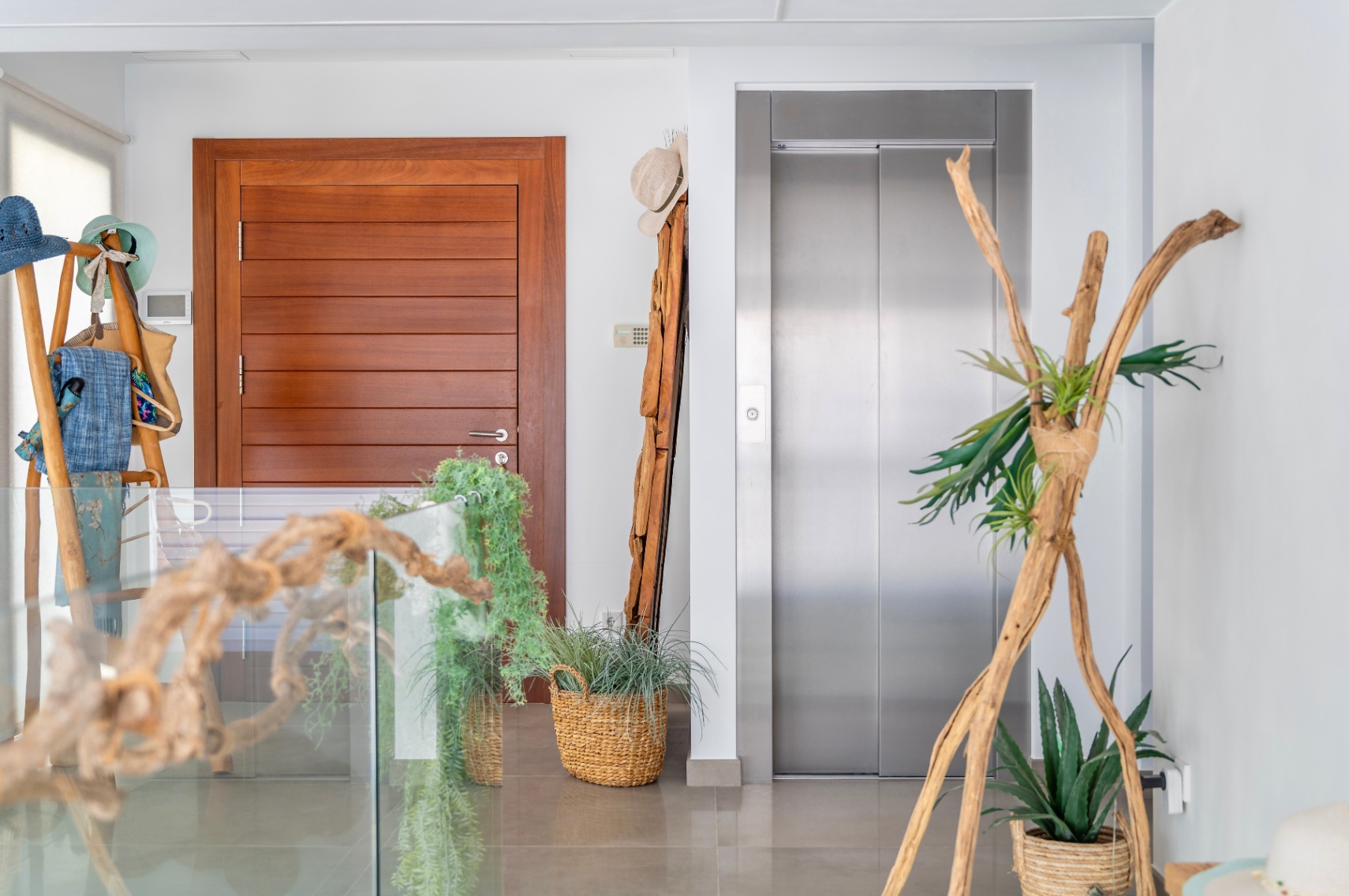 Palier intérieur moderne avec porte en bois élégante et ascenseur en acier inoxydable. Décoré d'éléments naturels comme du bois flotté, des plantes en paniers tressés et une balustrade en verre. Palier intérieur moderne avec porte en bois élégante et ascenseur en acier inoxydable. Décoré d'éléments naturels comme du bois flotté, des plantes en paniers tressés et une balustrade en verre.