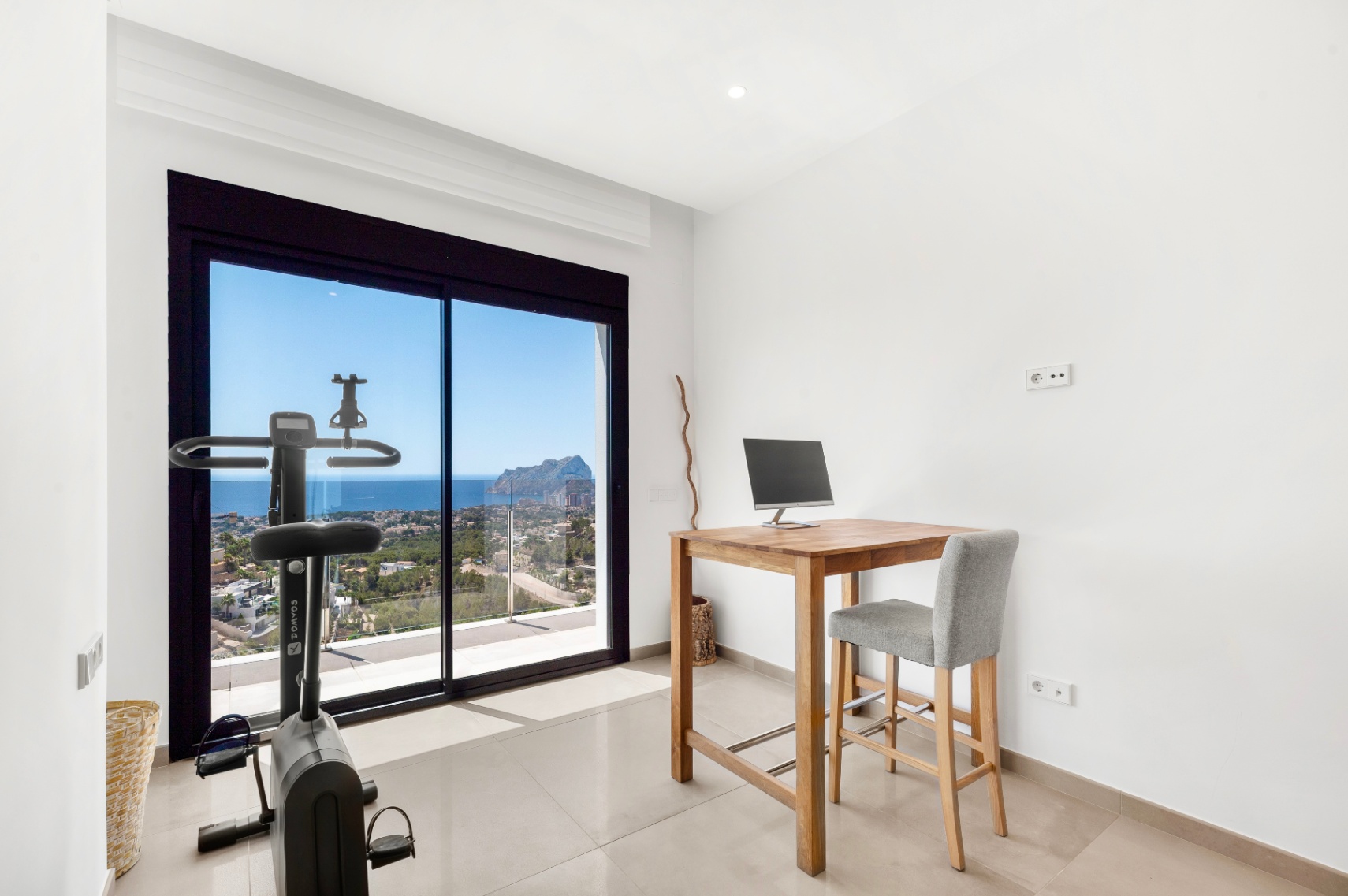 Pièce polyvalente avec bureau haut en bois et vélo d'appartement, offrant des vues imprenables sur la mer et le Peñon de Ifach à travers les grandes baies vitrées coulissantes. Pièce polyvalente avec bureau haut en bois et vélo d'appartement, offrant des vues imprenables sur la mer et le Peñon de Ifach à travers les grandes baies vitrées coulissantes.