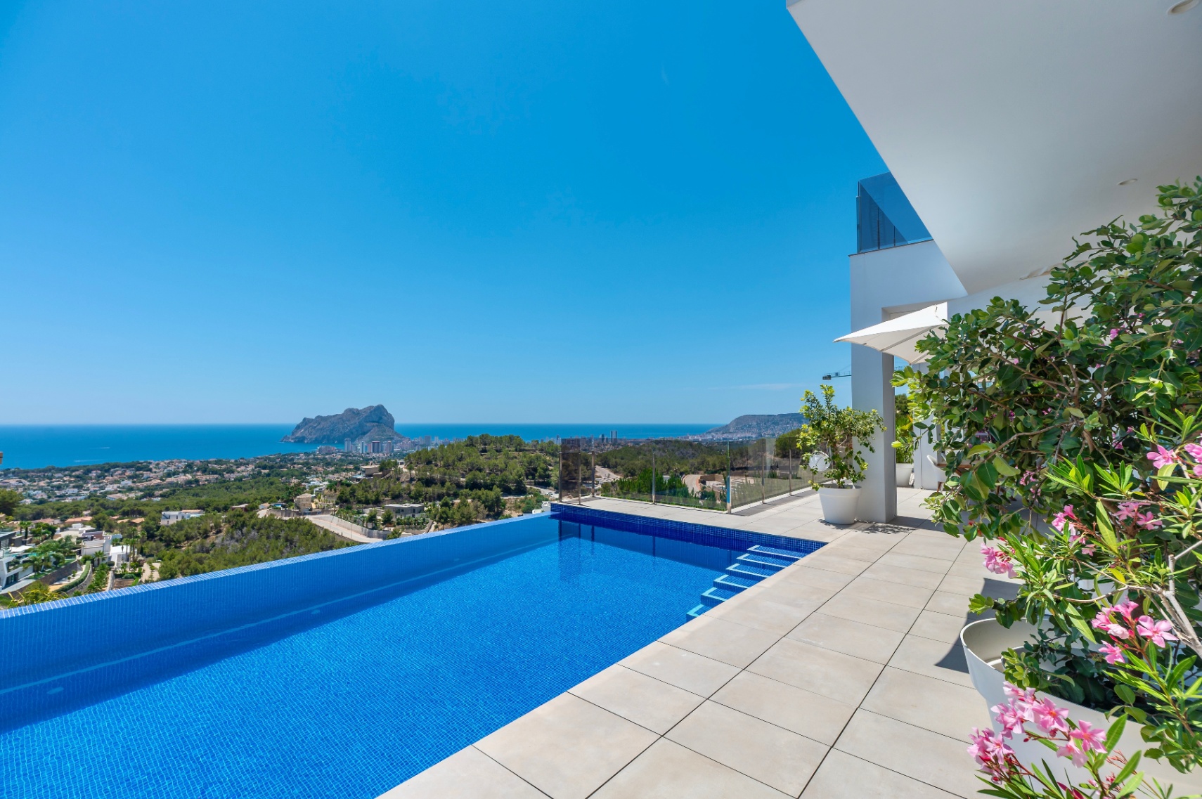 Piscine à débordement avec mosaïque bleue et vaste terrasse claire. Vues panoramiques imprenables sur la mer et le Peñon de Ifach, complétées par l'architecture moderne et la flore méditerranéenne. Piscine à débordement avec mosaïque bleue et vaste terrasse claire. Vues panoramiques imprenables sur la mer et le Peñon de Ifach, complétées par l'architecture moderne et la flore méditerranéenne.
