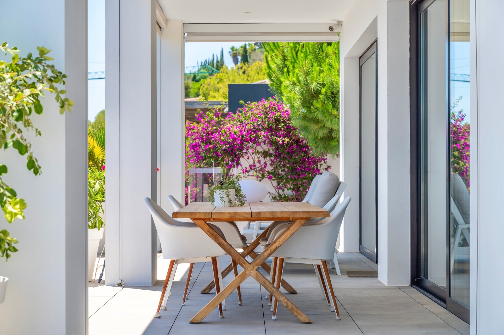 Terrasse couverte avec table à manger en bois et chaises blanches, encadrée par une végétation luxuriante et des bougainvilliers éclatants, idéale pour les repas en plein air. Terrasse couverte avec table à manger en bois et chaises blanches, encadrée par une végétation luxuriante et des bougainvilliers éclatants, idéale pour les repas en plein air.