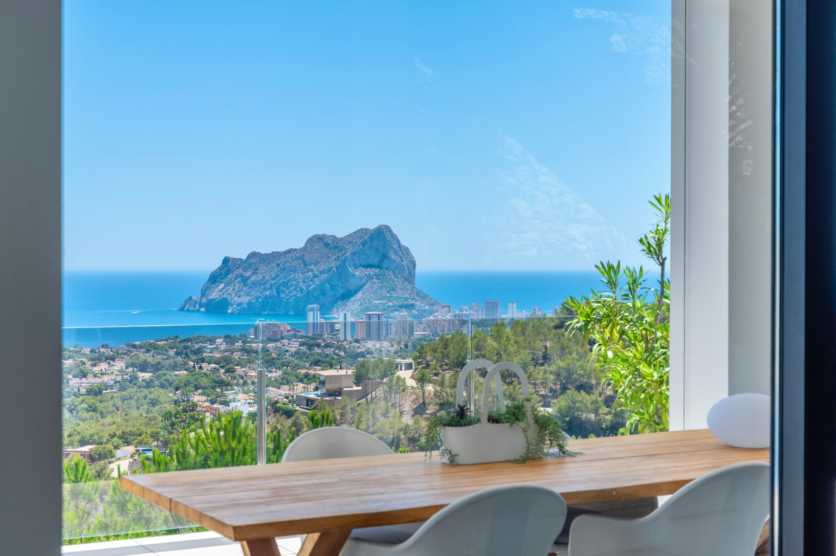 Terrasse repas extérieure avec table en bois et chaises blanches modernes, offrant une vue imprenable sur le Peñon de Ifach, la mer Méditerranée et la côte de Calpe. Terrasse repas extérieure avec table en bois et chaises blanches modernes, offrant une vue imprenable sur le Peñon de Ifach, la mer Méditerranée et la côte de Calpe.