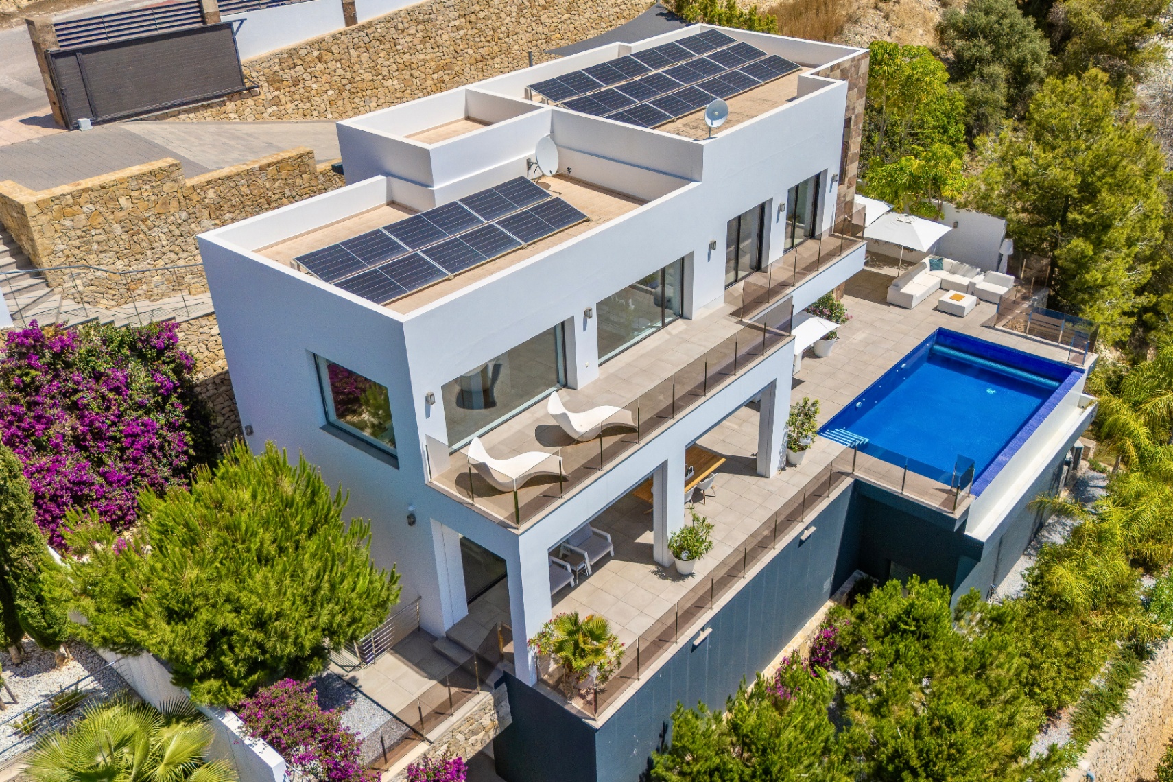 Vue aérienne d'une villa blanche moderne avec niveaux en terrasses, piscine rectangulaire et vastes espaces extérieurs. Panneaux solaires sur les toits plats, entourée d'un paysage méditerranéen luxuriant. Vue aérienne d'une villa blanche moderne avec niveaux en terrasses, piscine rectangulaire et vastes espaces extérieurs. Panneaux solaires sur les toits plats, entourée d'un paysage méditerranéen luxuriant.