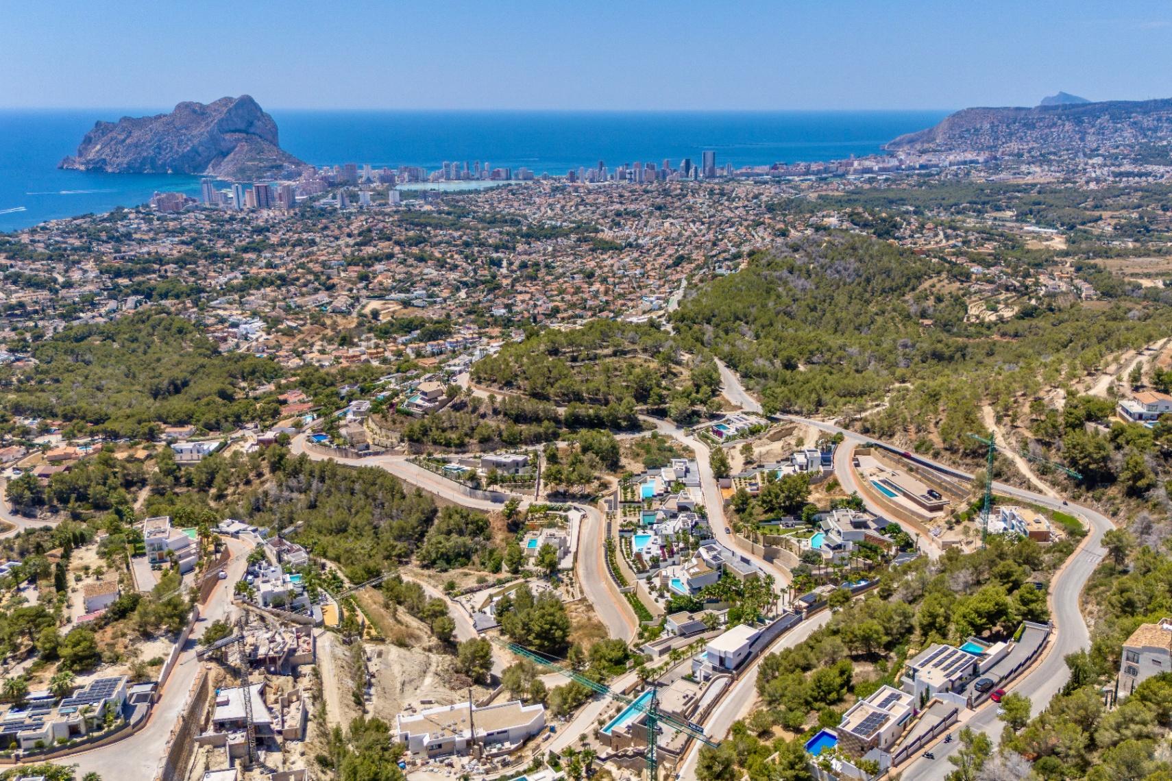 Vue aérienne panoramique de Calpe, avec le Peñon de Ifach, la côte et un quartier résidentiel de villas et piscines niché dans des collines verdoyantes et des routes sinueuses. Vue aérienne panoramique de Calpe, avec le Peñon de Ifach, la côte et un quartier résidentiel de villas et piscines niché dans des collines verdoyantes et des routes sinueuses.