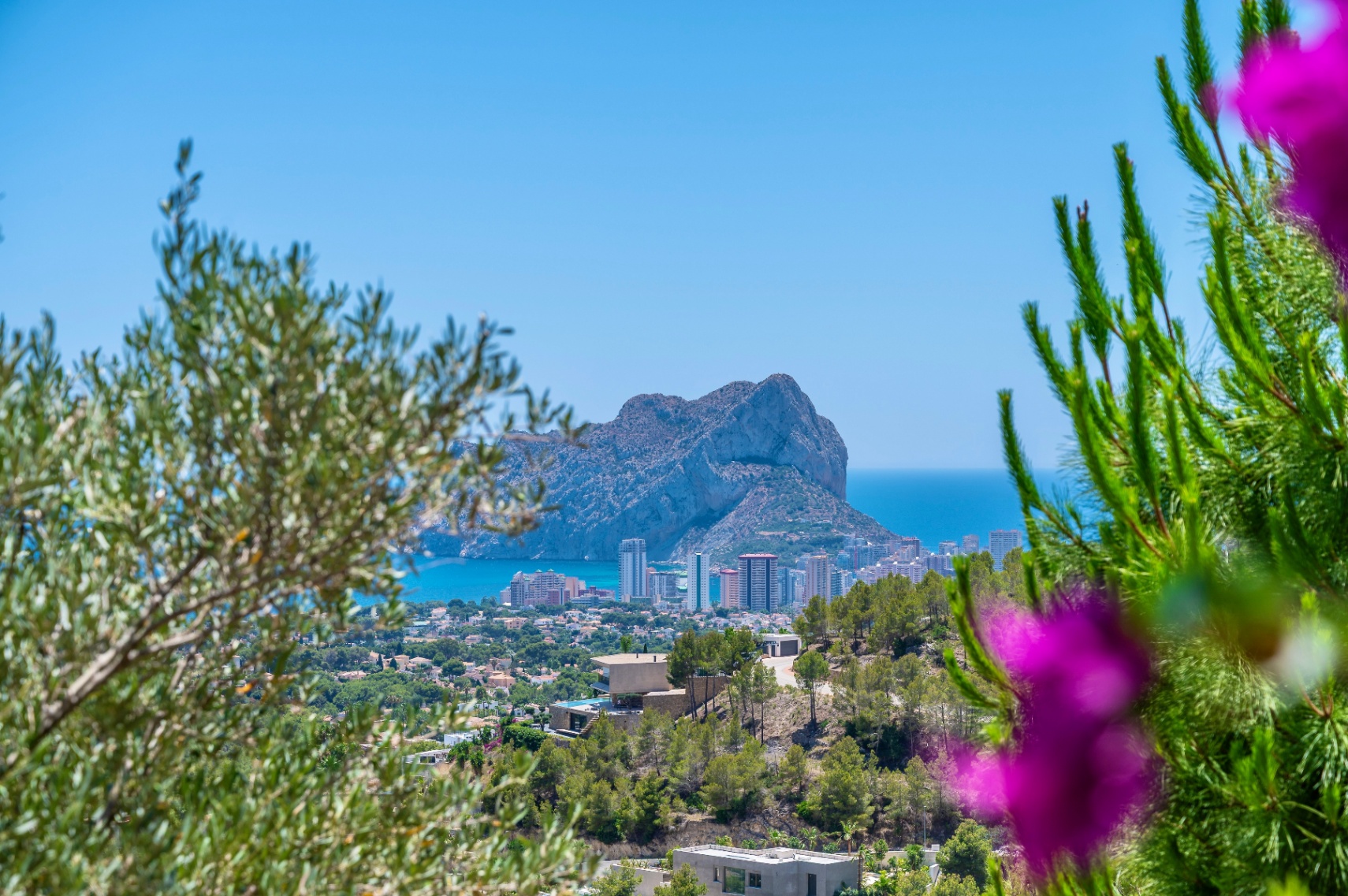 Vue panoramique sur le Peñón de Ifach et la côte de Calpe, encadrée par la végétation méditerranéenne, avec des villas modernes sur la colline. Vue panoramique sur le Peñón de Ifach et la côte de Calpe, encadrée par la végétation méditerranéenne, avec des villas modernes sur la colline.