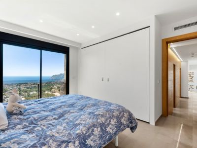Chambre avec portes coulissantes vitrées pleine hauteur, offrant des vues panoramiques sur la mer et la ville. Intègre des armoires blanches encastrées et un sol carrelé clair.