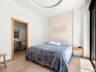 Chambre lumineuse avec lit double, un mur d'accent décoré de silhouettes de bâtiments et accès à une salle de bain attenante. Porte coulissante vitrée menant directement à une terrasse extérieure.