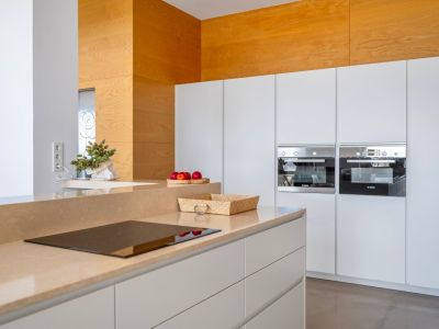 Cuisine moderne avec plan de travail couleur sable et plaque à induction intégrée. Deux fours Bosch encastrés et un mur décoratif en bois clair.