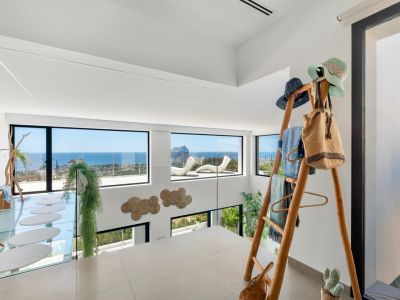 Étage supérieur avec carrelage clair et balustrade en verre. Vues panoramiques sur la mer et le Peñon de Ifach par de grandes fenêtres. Comprend une passerelle en verre à marches ovales et un porte-manteau en bois.