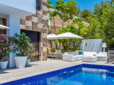Grande terrasse avec piscine en mosaïque bleue et mobilier extérieur blanc sous parasols, agrémentée d'une façade en pierre et d'une végétation méditerranéenne luxuriante.