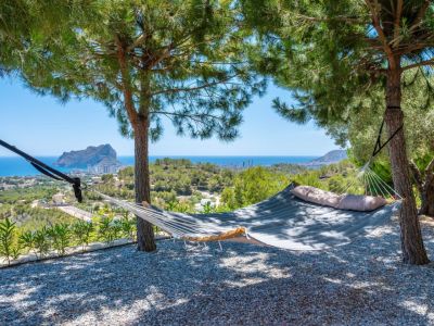 Hamac rembourré installé sous les pins, offrant un espace de détente avec des vues panoramiques sur la mer Méditerranée et le majestueux Peñon de Ifach. Sol en gravier.