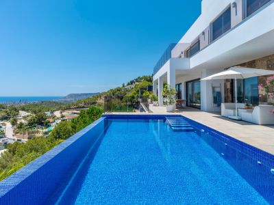 Piscine à débordement en mosaïque bleue avec marches intégrées, jouxtant une terrasse spacieuse avec mobilier de salon et vues panoramiques sur la côte et la ville.
