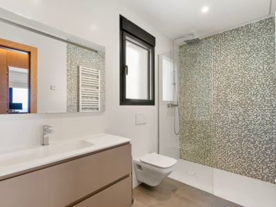 Salle de bain moderne avec douche à l'italienne et mur en mosaïque aux tons terreux. Elle dispose d'un meuble-lavabo suspendu avec vasque intégrée, toilettes murales et fenêtre à cadre noir.