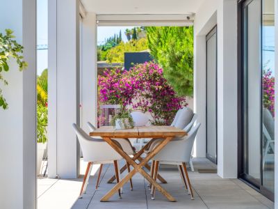 Terrasse couverte avec table à manger en bois et chaises blanches, encadrée par une végétation luxuriante et des bougainvilliers éclatants, idéale pour les repas en plein air.
