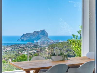 Terrasse repas extérieure avec table en bois et chaises blanches modernes, offrant une vue imprenable sur le Peñon de Ifach, la mer Méditerranée et la côte de Calpe.