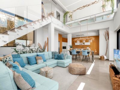 Vaste espace de vie ouvert avec canapé sectionnel bleu clair, escalier moderne en verre et cuisine aux accents de bois chaleureux, baigné de lumière naturelle.