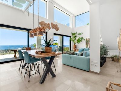 Vaste salon-salle à manger ouvert avec hauts plafonds, grandes fenêtres et un lustre unique en branches. Profitez de vues panoramiques sur la mer, la côte et le Peñón de Ifach depuis cet intérieur lumineux.