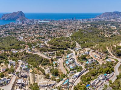 Vue aérienne panoramique de Calpe, avec le Peñon de Ifach, la côte et un quartier résidentiel de villas et piscines niché dans des collines verdoyantes et des routes sinueuses.