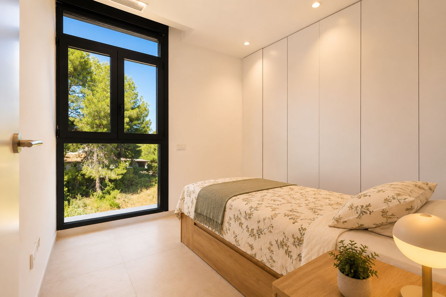 Chambre lumineuse avec lit simple à base en bois, placards intégrés blancs et grande fenêtre noire offrant des vues naturelles. Éclairage encastré au plafond. Chambre lumineuse avec lit simple à base en bois, placards intégrés blancs et grande fenêtre noire offrant des vues naturelles. Éclairage encastré au plafond.