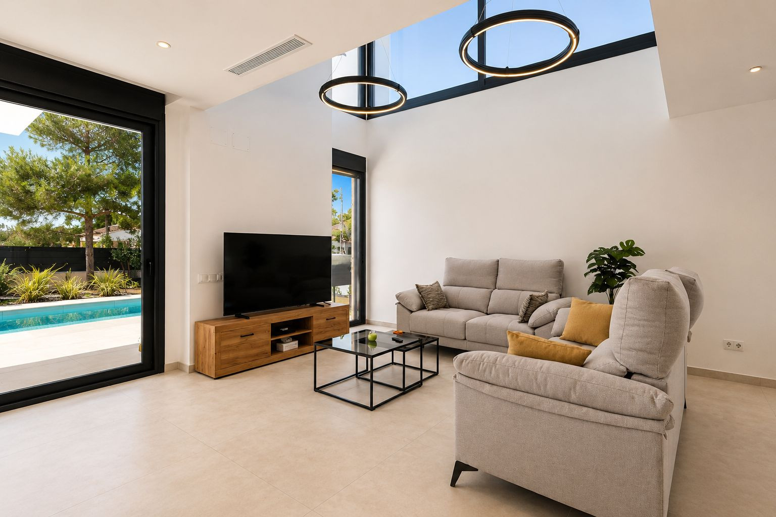 Vaste salon avec plafond à double hauteur, puits de lumière et suspensions circulaires modernes. Une grande porte vitrée s'ouvre sur la piscine privée et le jardin. Vaste salon avec plafond à double hauteur, puits de lumière et suspensions circulaires modernes. Une grande porte vitrée s'ouvre sur la piscine privée et le jardin.