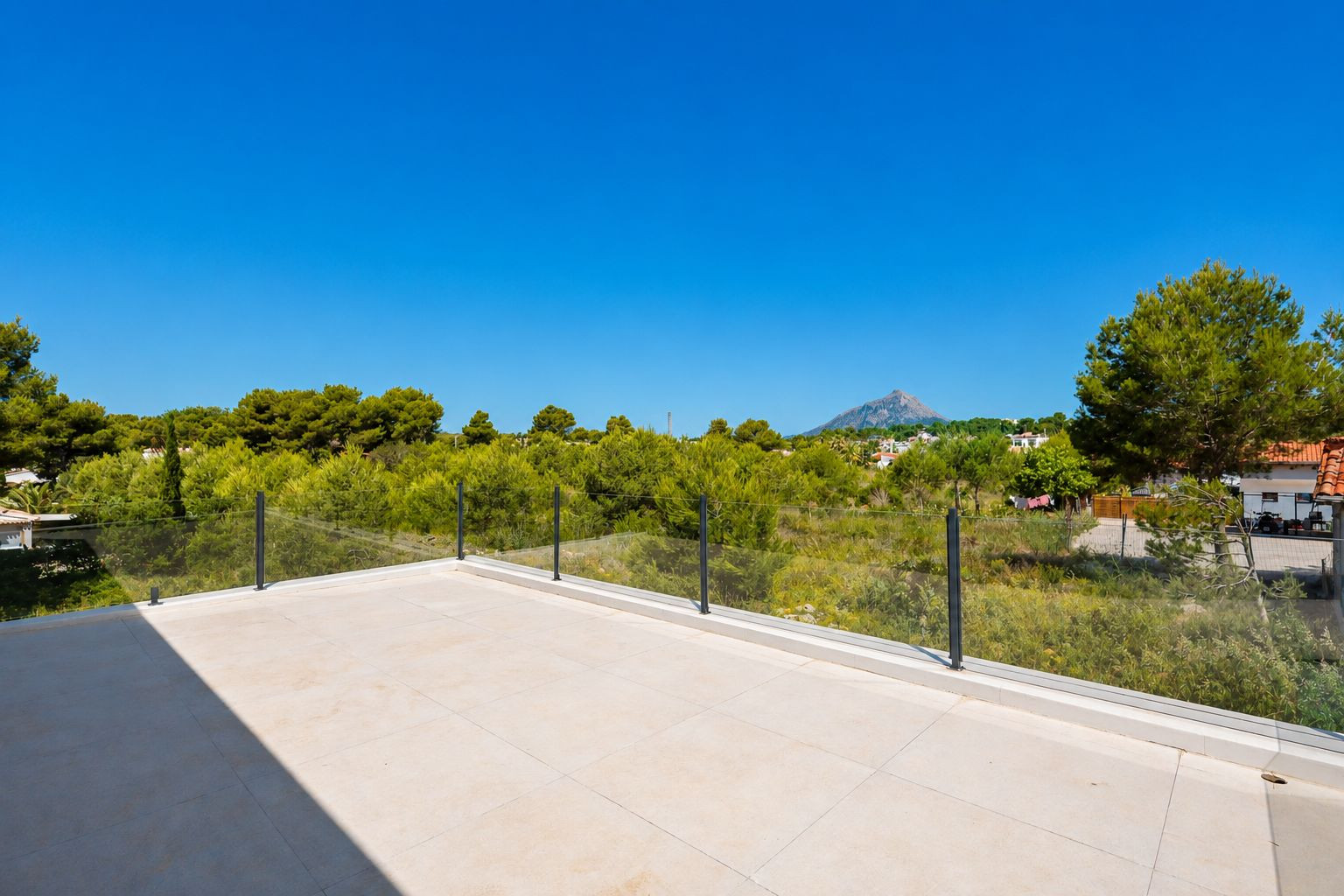 Vaste terrasse supérieure avec carrelage clair en grès cérame et garde-corps en verre, offrant des vues sur la végétation méditerranéenne et le profil montagneux lointain. Vaste terrasse supérieure avec carrelage clair en grès cérame et garde-corps en verre, offrant des vues sur la végétation méditerranéenne et le profil montagneux lointain.