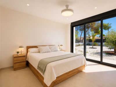 Chambre avec lit en bois, tables de chevet assorties et accès direct à un jardin de gravier par de grandes portes coulissantes vitrées. Éclairage encastré et ventilateur de plafond.