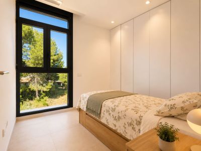 Chambre lumineuse avec lit simple à base en bois, placards intégrés blancs et grande fenêtre noire offrant des vues naturelles. Éclairage encastré au plafond.