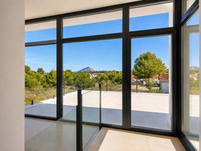 Grande baie vitrée à cadres sombres et balustrade en verre, reliant l'intérieur à une terrasse carrelée avec vue sur la pinède et la montagne.