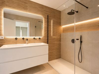 Salle de bain moderne avec double vasque suspendue, robinetterie noire murale et miroir éclairé. Douche à l'italienne avec paroi vitrée et carrelage effet bois texturé.