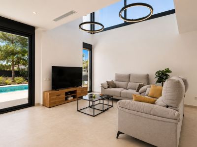 Vaste salon avec plafond à double hauteur, puits de lumière et suspensions circulaires modernes. Une grande porte vitrée s'ouvre sur la piscine privée et le jardin.