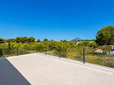 Vaste terrasse supérieure avec carrelage clair en grès cérame et garde-corps en verre, offrant des vues sur la végétation méditerranéenne et le profil montagneux lointain.