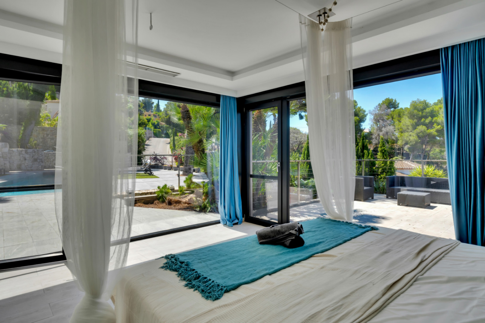 Chambre lumineuse avec accès direct à une vaste terrasse extérieure, piscine et vues verdoyantes par de grandes baies vitrées.