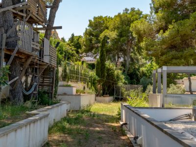Cabane en bois rustique intégrée à des pins matures, avec un hamac. Le jardin en terrasses présente des murs en béton, une végétation dense et une pergola moderne.