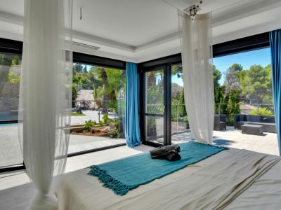 Chambre lumineuse avec accès direct à une vaste terrasse extérieure, piscine et vues verdoyantes par de grandes baies vitrées.