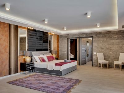 Chambre spacieuse au design moderne avec mur effet pierre texturé, tête de lit capitonnée et éclairage LED intégré. Accès direct à un dressing et une salle de bain attenante.