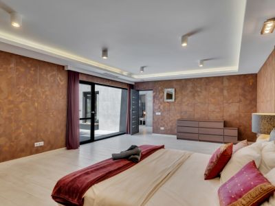 Chambre spacieuse avec murs texturés couleur cuivre et sol clair. Elle bénéficie d'un accès direct à un patio extérieur par une grande porte vitrée coulissante et d'un éclairage de plafond moderne.