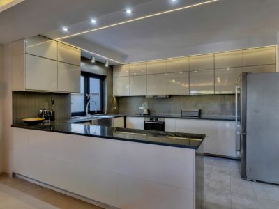 Cuisine moderne avec armoires crème laquées, plans de travail en granit noir et appareils intégrés. Éclairage LED linéaire et encastré au plafond.