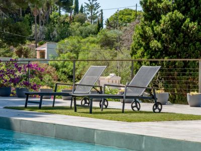 Deux transats contemporains sur gazon synthétique au bord de la piscine, avec une balustrade métallique et une végétation méditerranéenne luxuriante en arrière-plan.