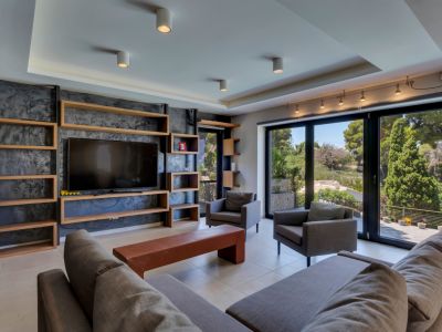 Grand salon doté d'une bibliothèque en bois sur mesure intégrée autour de la télévision sur un mur texturé sombre. De larges portes vitrées encadrent des vues verdoyantes, complétant les sièges gris modernes.
