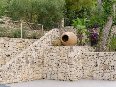 Jardin en terrasses avec murs en pierres sèches, escaliers intégrés et flore méditerranéenne variée. Une grande jarre décorative et des cactus soulignent l'esthétique naturelle et rustique.