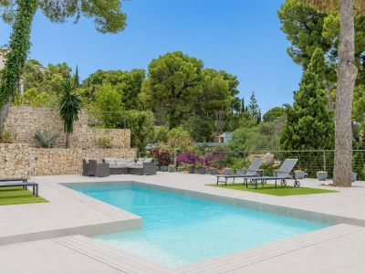Piscine privée rectangulaire bordée d'une vaste terrasse carrelée claire, avec salon de jardin et mur en pierre naturelle au cœur d'une végétation luxuriante.