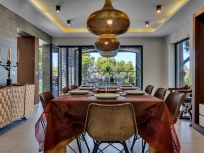 Salle à manger élégante avec des suspensions en bronze ouvragées, un buffet en bois texturé et de grandes fenêtres offrant une vue paisible sur la verdure luxuriante.